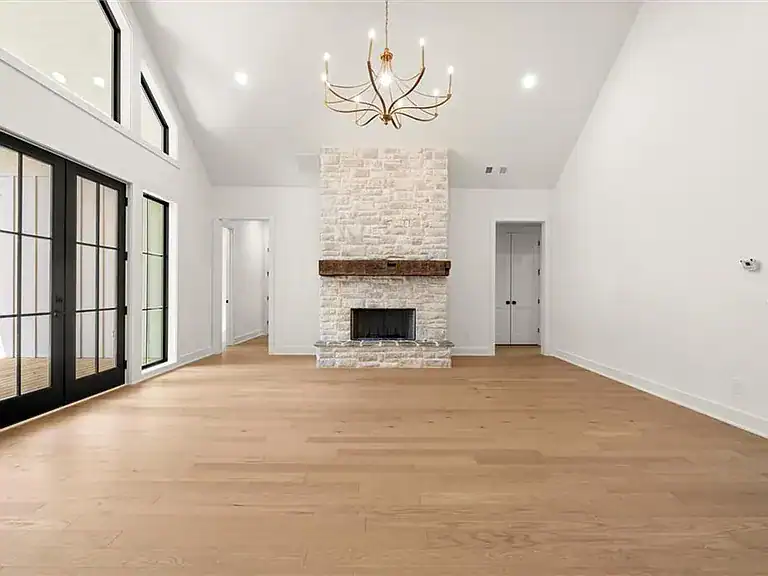 d7b5fb672fd6b80d2c8ebc5b72dea33f-cc_ft_768 Modern living room with white walls, hardwood floors, and a stone fireplace featuring a wooden mantel. Large windows and a chandelier enhance the space.